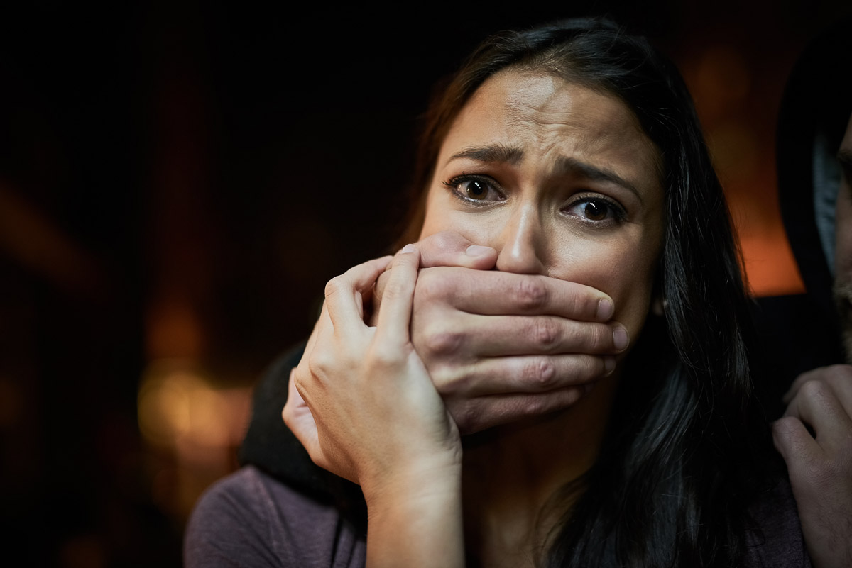 Portrait of a frightened young woman with her assailants hand ov